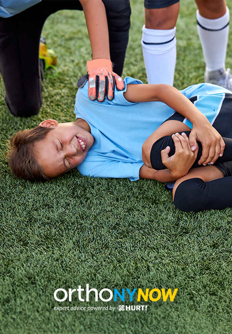 kid laying on ground holding knee, comforting hand on shoulder; OrthoNYNow logo