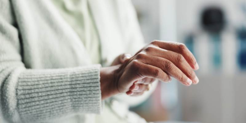 A person wearing a light green sweater gently massages their right wrist with their left hand, suggesting discomfort or pain in the wrist—raising the question: can cold weather make arthritis worse?