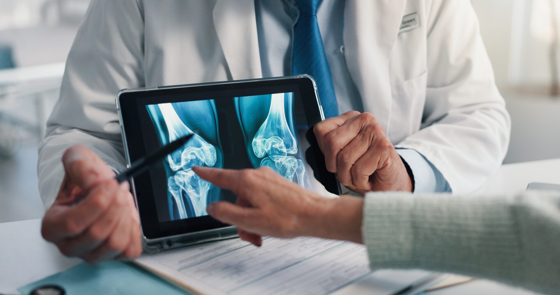 An arthritis specialist goes over imaging with a patient, showing them the damage to the joints before creating a tailored treatment plan to begin managing pain and reducing inflammation, protecting the patient from the effects of cold weather.